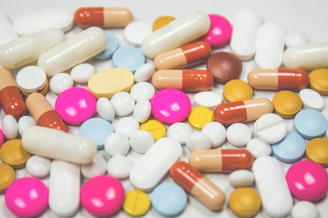 A mix of colorful pills and capsules scattered on a white surface, representing pharmaceuticals.