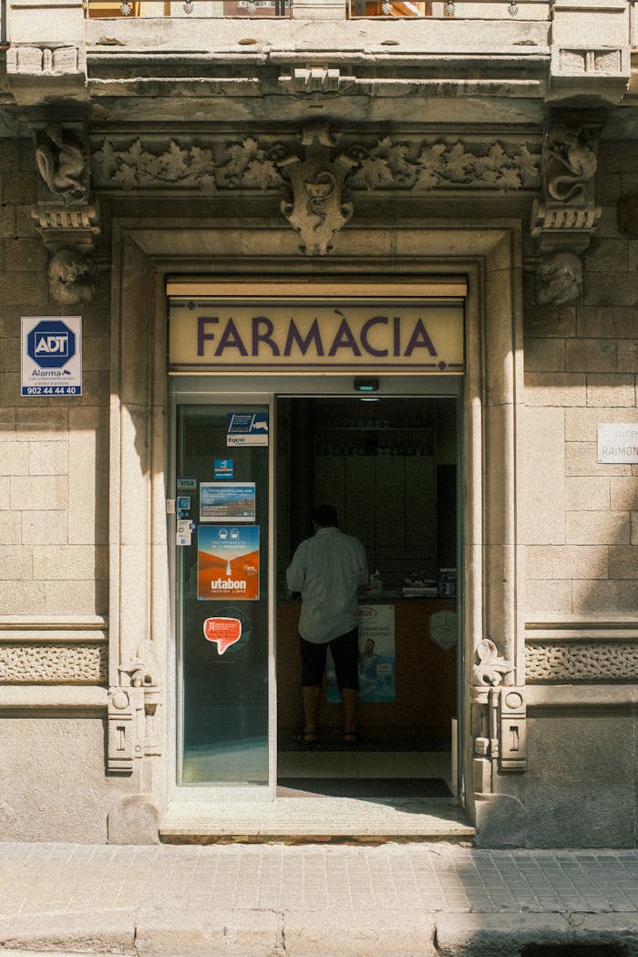 Architectural details of a historic pharmacy entrance in Madrid, Spain, featuring a lone customer inside.